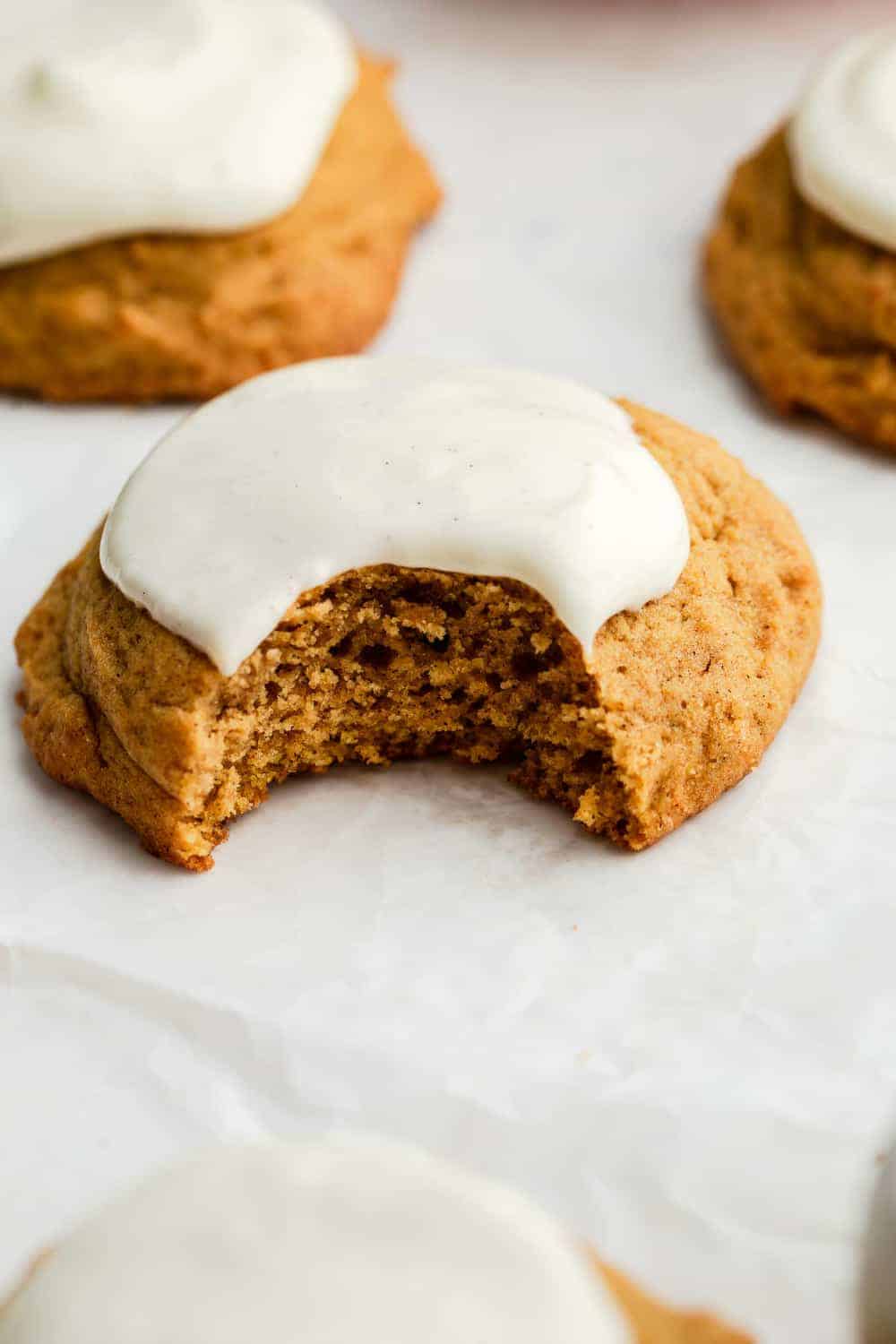 Close up of a pumpkin cookie topped with cream cheese frosting with a bite taken out of it