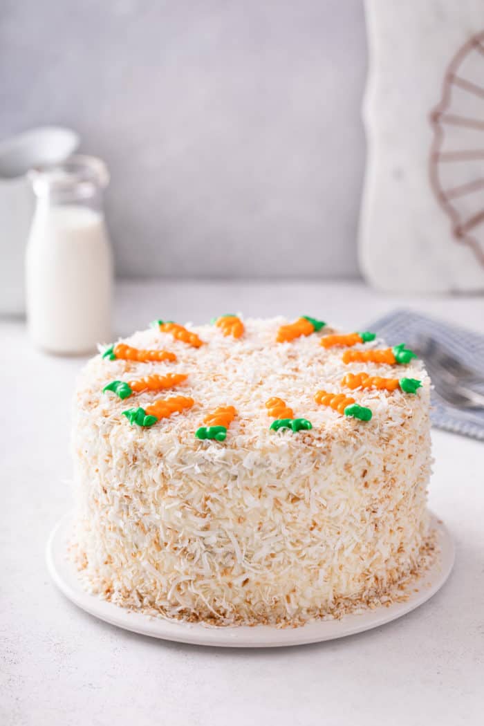 Assembled carrot cake, coated with toasted coconut and decorated with icing carrots on the top.