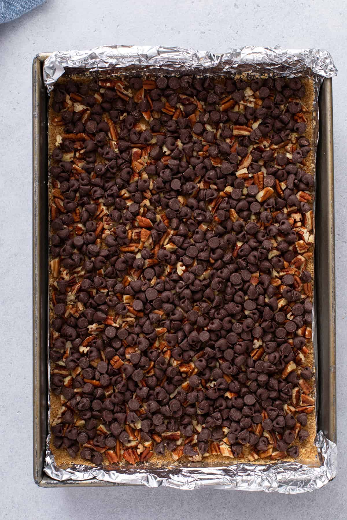 Chopped pecans and chocolate chips layered on top of a graham cracker crust.