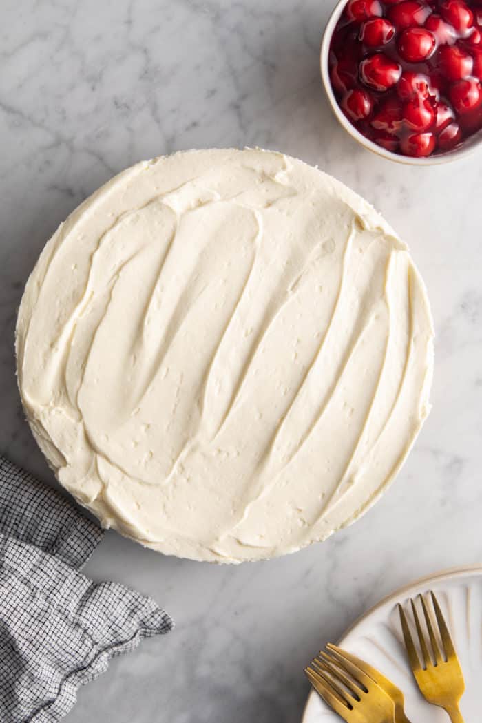 Assembled and chilled no-bake cheesecake next to a bowl of cherry pie filling.