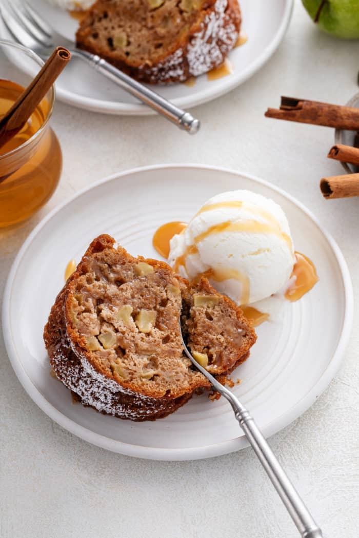 Fork cutting a bite from the corner of a slice of easy apple bundt cake on a white plate.