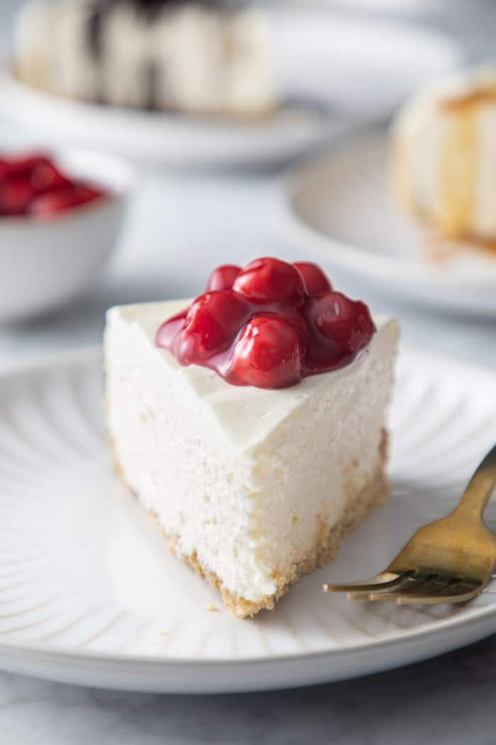 Front view of a slice of no-bake cheesecake topped with cherry pie filling on a white plate.