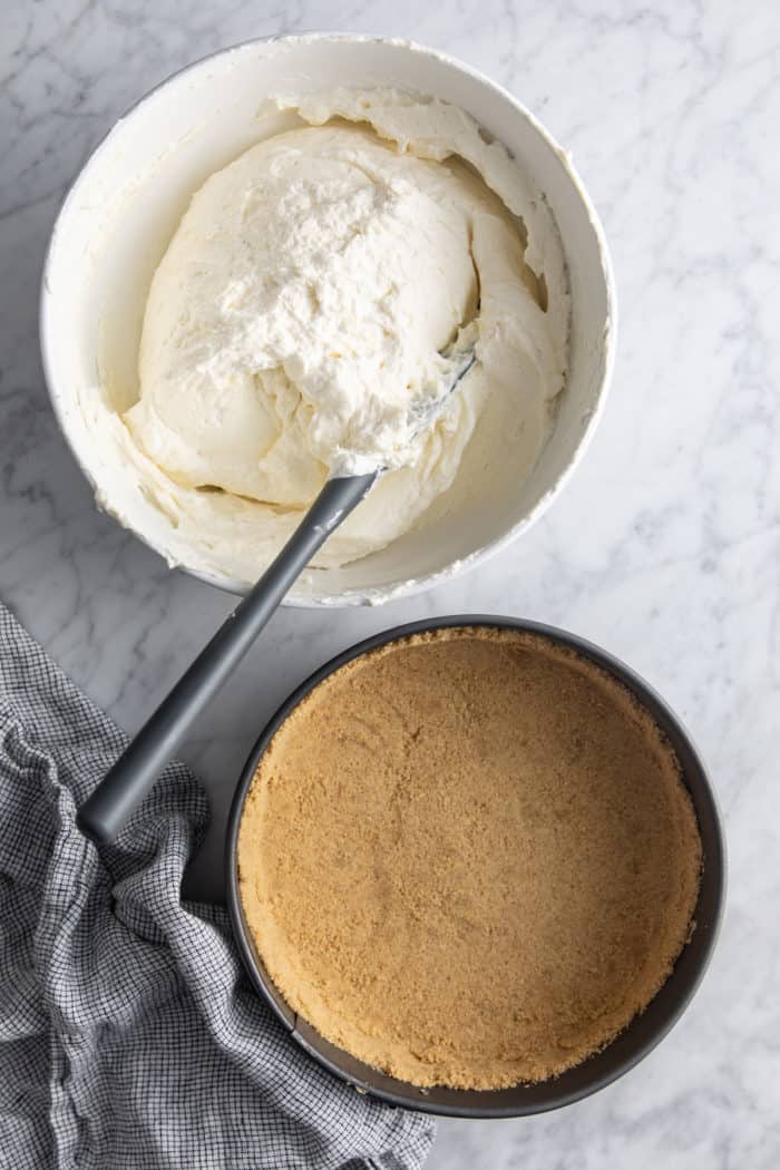 No-bake cheesecake filling in a white bowl next to a graham cracker crust in a springform pan.