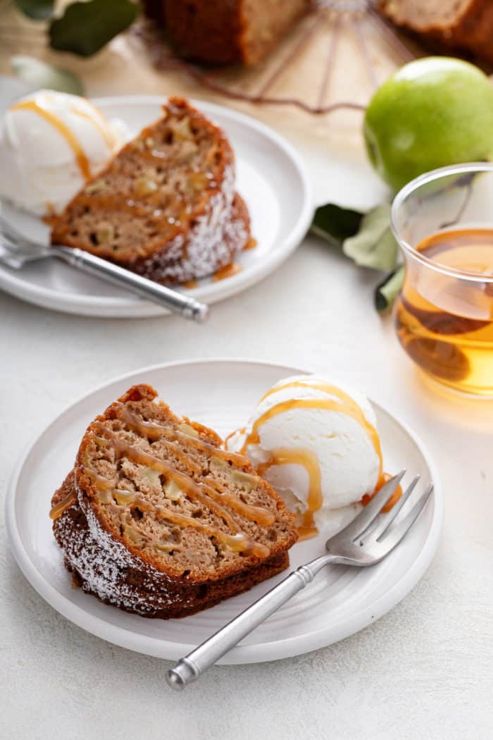 Slice of easy apple bundt cake and a scoop of ice cream on a white plate, both drizzled with caramel sauce.