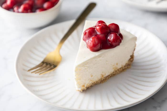 Slice of no-bake cheesecake topped with cherry pie filling on a white plate.