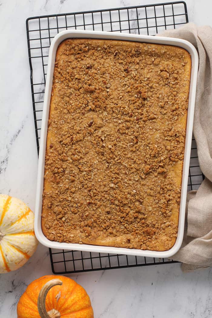 Baked pumpkin cheesecake bars in a white baking dish, set on a wire rack to cool