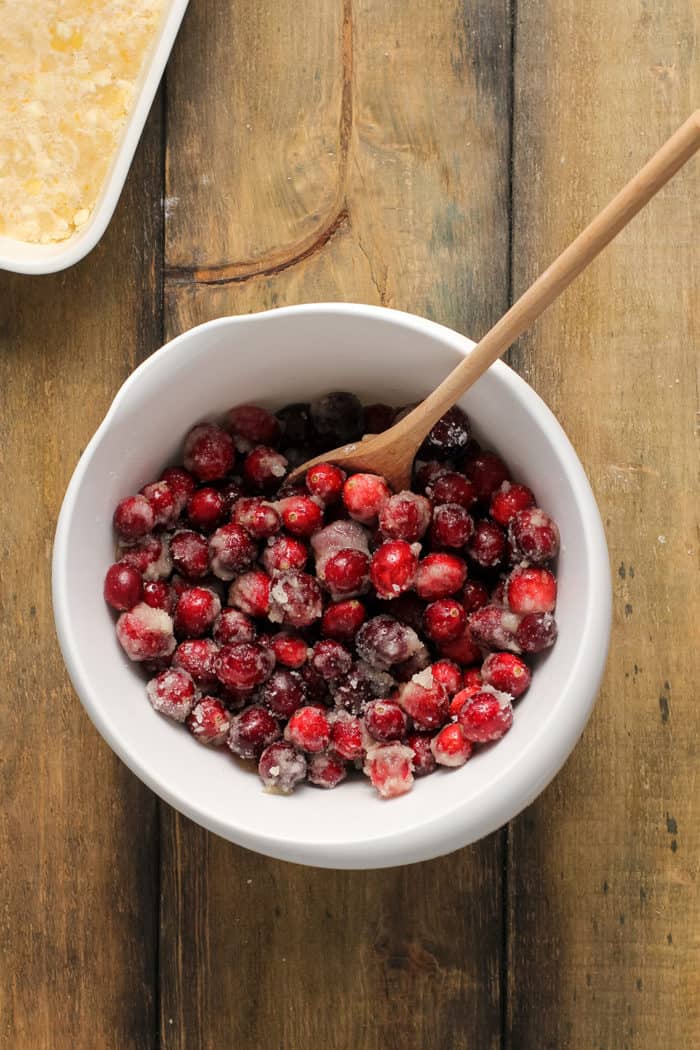 Wooden spoon stirring cranberry filling for crumb bars in a white mixing bowl