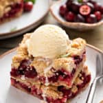 Two cranberry crumb bars stacked on a plate and topped with a scoop of vanilla ice cream