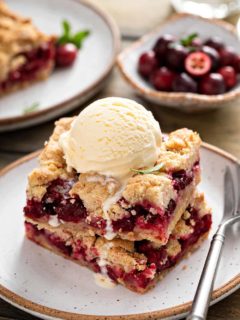 Two cranberry crumb bars stacked on a plate and topped with a scoop of vanilla ice cream