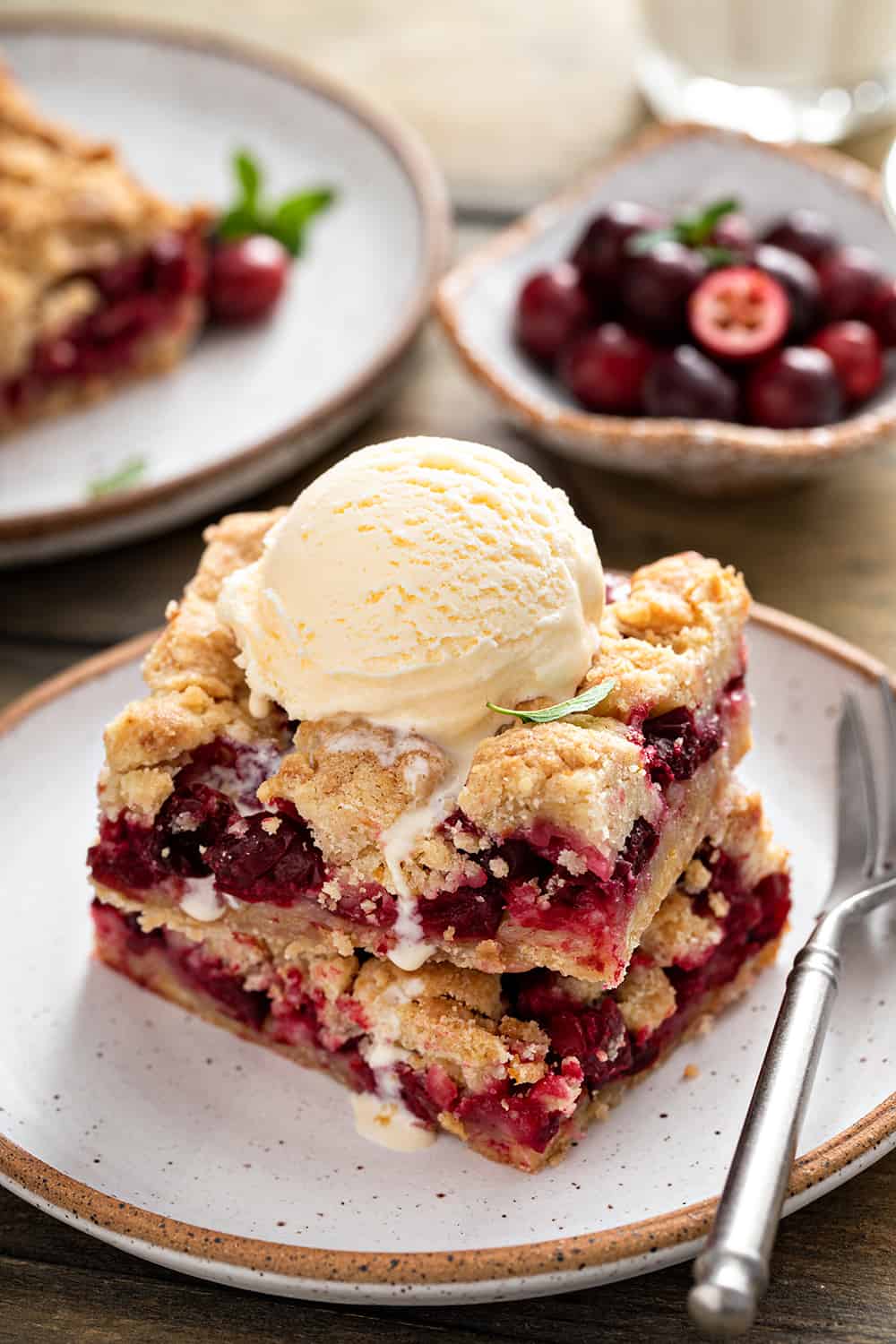 Two cranberry crumb bars stacked on a plate and topped with a scoop of vanilla ice cream