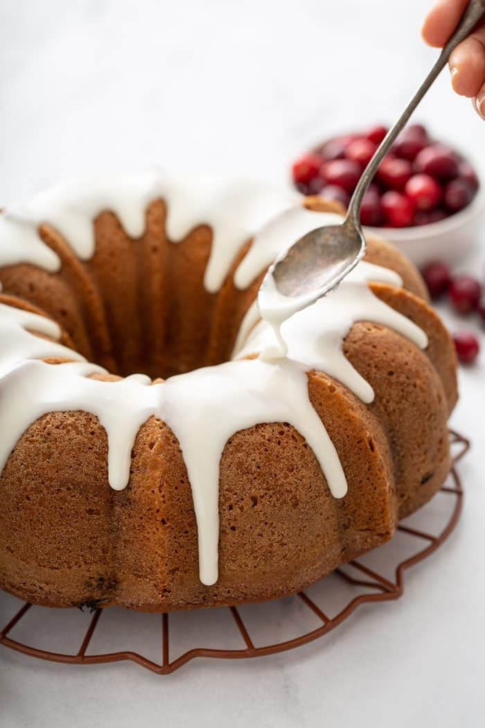 Spoon pouring glaze over a baked cranberry orange bundt cake