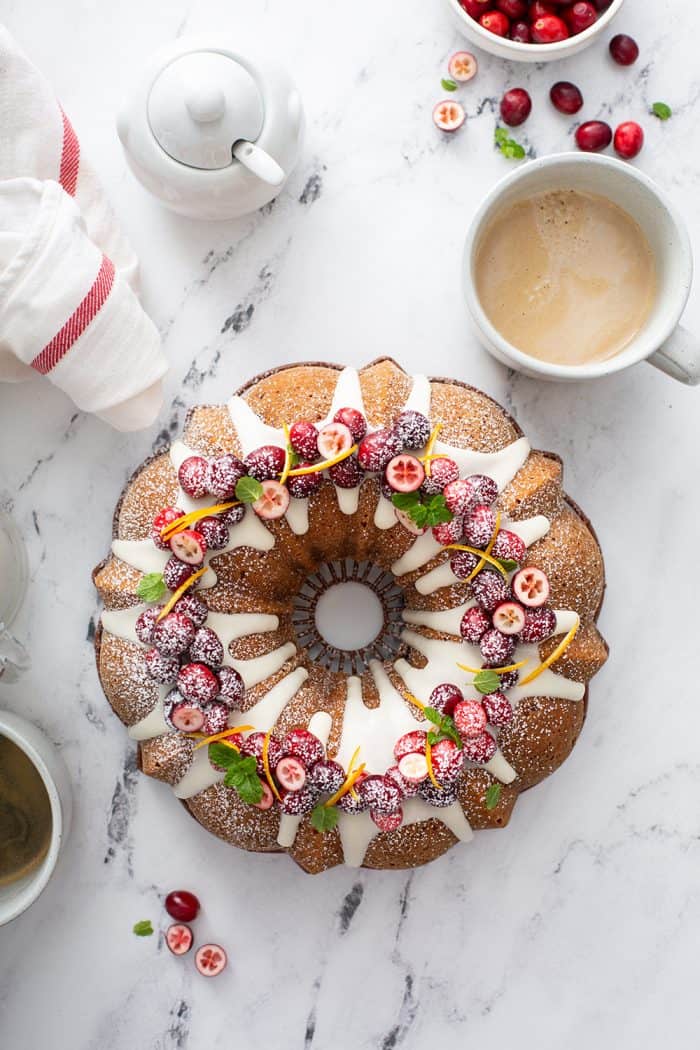 Overhead view of cranberry orange cake topped with fresh cranberries, set on a marble countertop