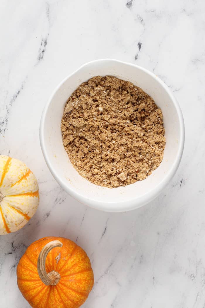 Pumpkin cheesecake bar crust mixed together in a white mixing bowl on a marble countertop