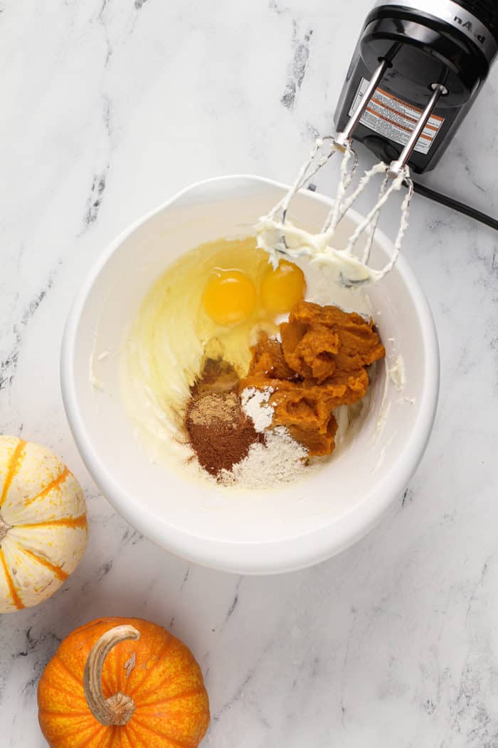 Ingredients for pumpkin cheesecake bar filling about to be mixed together in a white mixing bowl