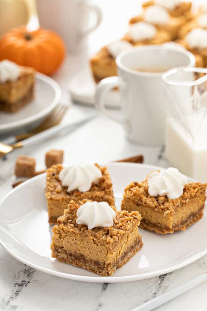 White plate with three pumpkin cheesecake bars in front of a cup of coffee
