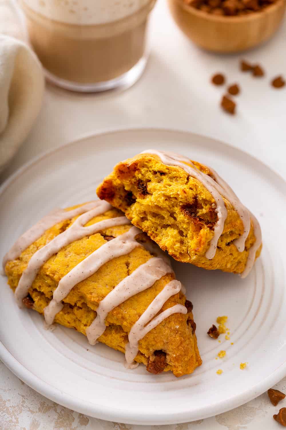 Two pumpkin scones on a white plate. One of them has been broken in half to show the inside of the scone
