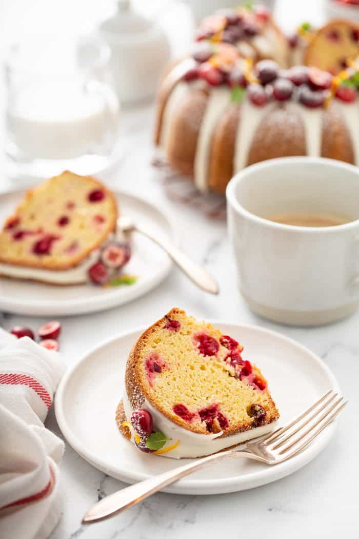 Two white plates with slices of cranberry orange bundt cake with a full bundt cake in the background