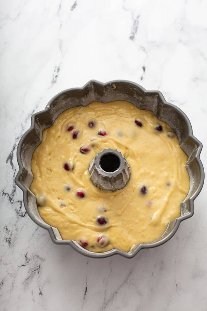 Unbaked cranberry orange cake in a bundt pan set on a marble counter