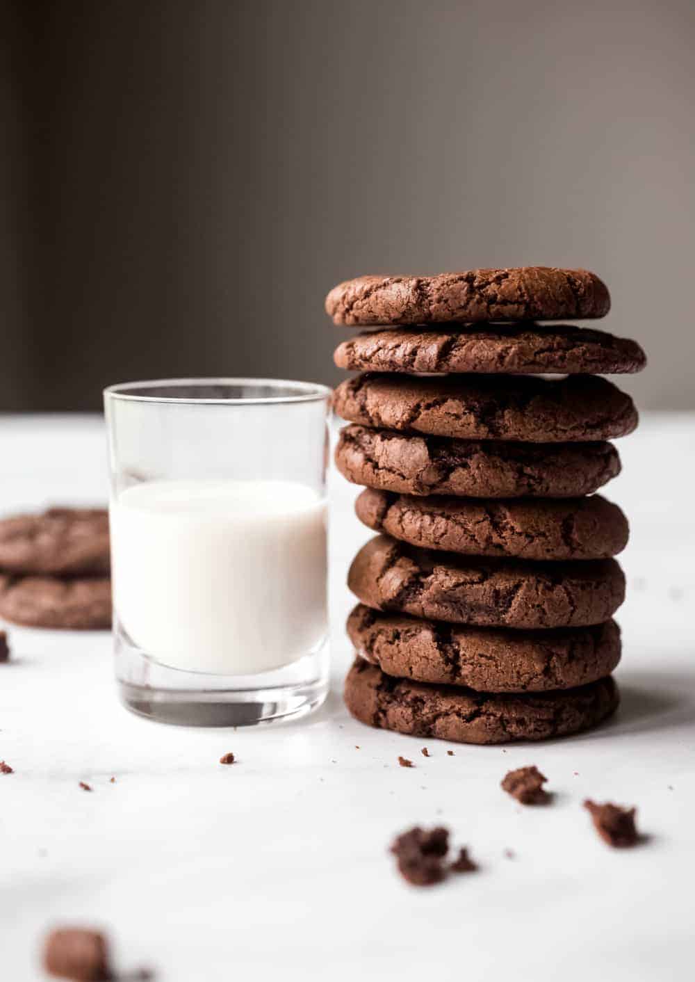 Side view of several mint chocolate cookies stacked next to a glass of milk