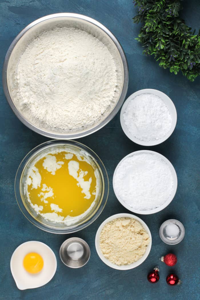 Ingredients for almond crescent cookies arranged on a blue countertop.