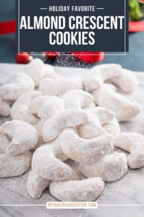 Almond crescent cookies arranged in a pile on a marble board. Powdered sugar is being dusted over the top of the cookies. Text overlay includes recipe name.