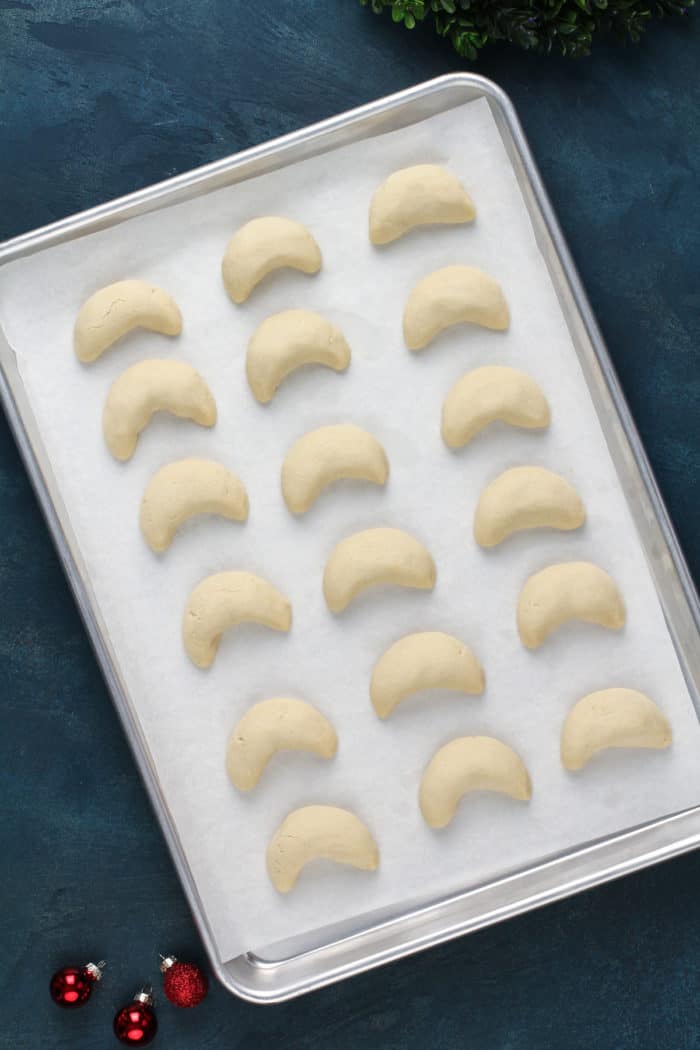 Baked almond crescent cookies cooling on a parchment-lined baking sheet.