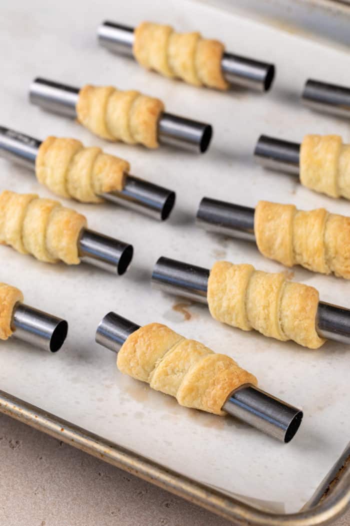 Baked clothespin cookie shells on mini cannoli forms on a parchment-lined baking sheet.