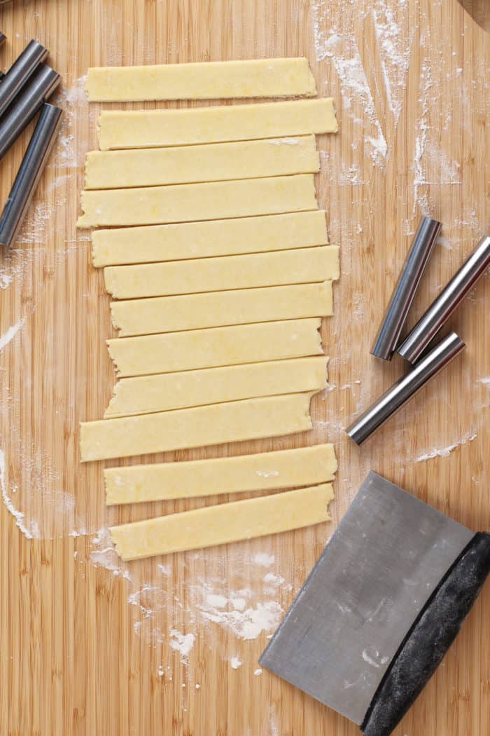 Strips of clothespin cookie dough on a flour-dusted wooden board.
