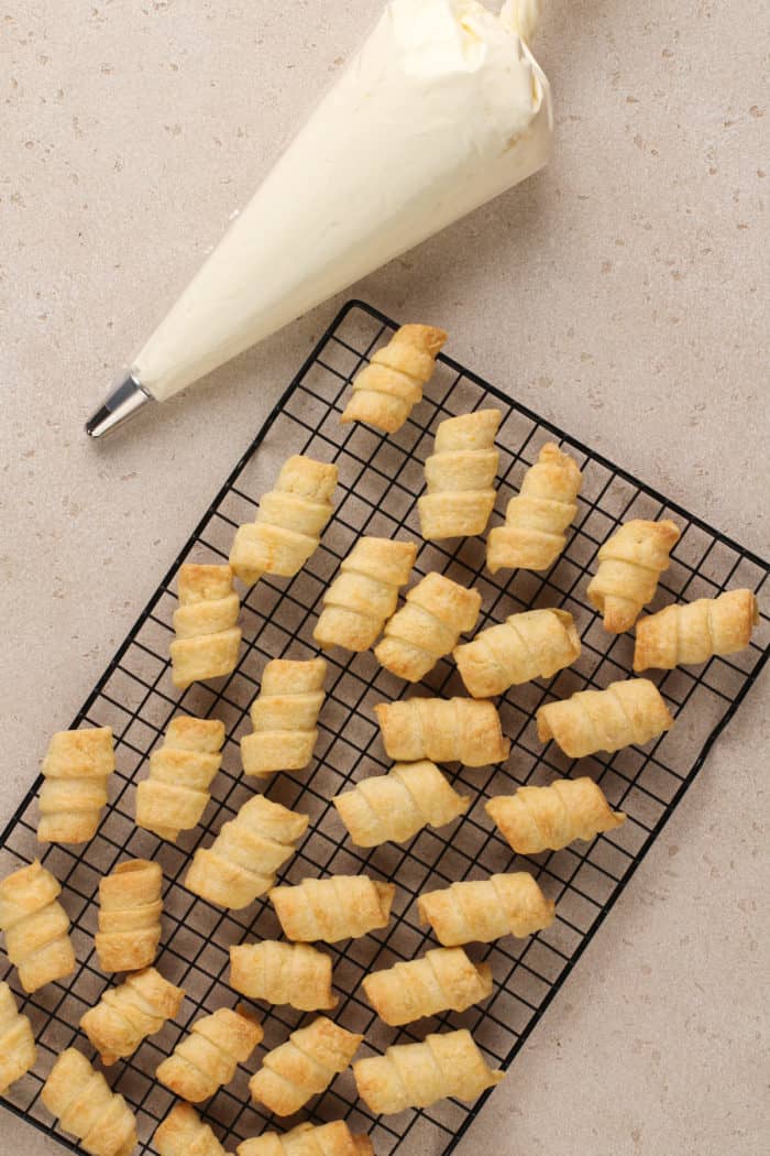 Clothespin cookie shells on a wire rack next to a piping bag filled with buttercream filling.