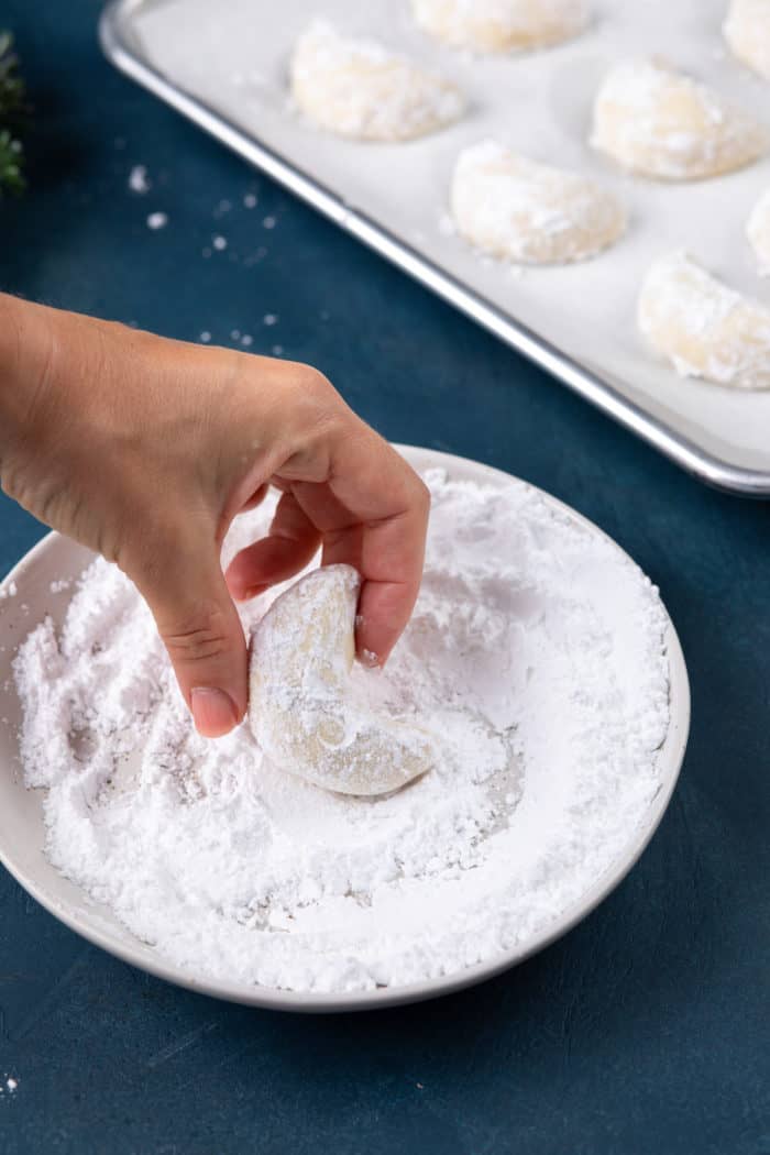 Hand coating an almond crescent cookie in powdered sugar.