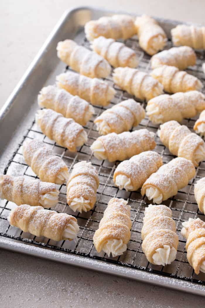 Clothespin cookies dusted with powdered sugar arranged on a wire rack over a rimmed baking sheet.