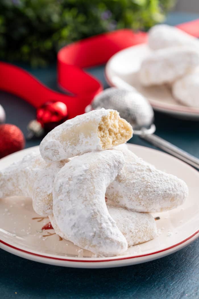 Pile of almond crescent cookies on a plate, with the top cookie broken in half.