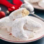 Almond crescent cookies piled on a plate. The top cookie is broken in half to show the texture of the inside.