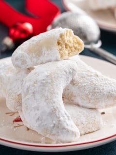 Almond crescent cookies piled on a plate. The top cookie is broken in half to show the texture of the inside.
