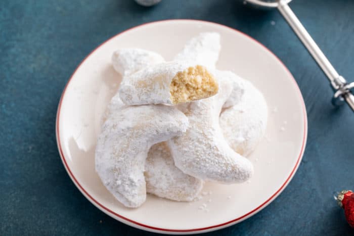 Halved almond crescent cookie on top of a pile of almond crescents on a plate.