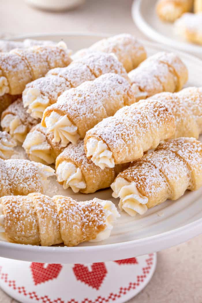 Clothespin cookies dusted with powdered sugar piled on a white cake plate.