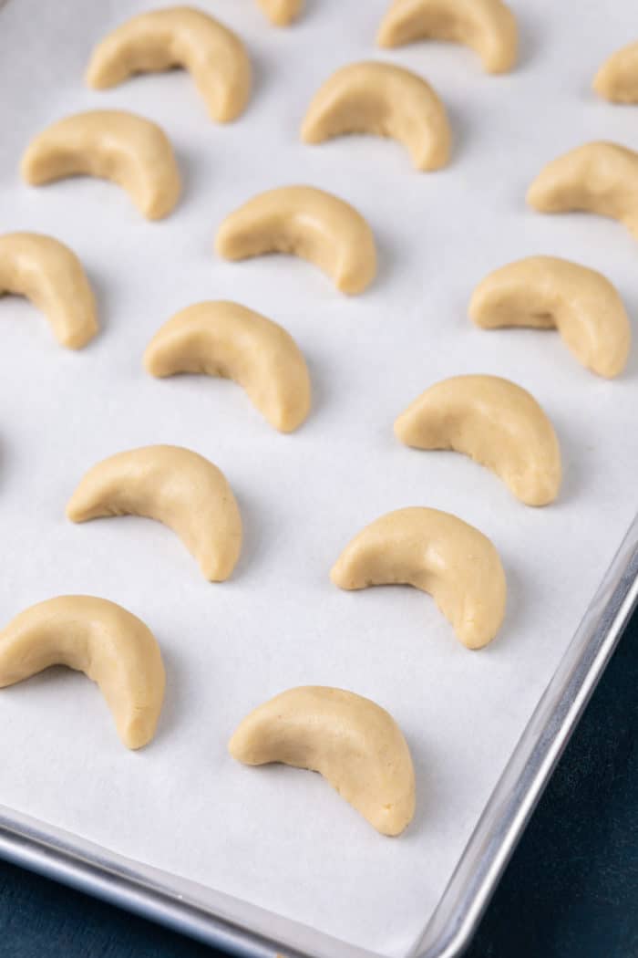 Shaped almond crescent cookies on a parchment-lined baking sheet, ready to go in the oven.