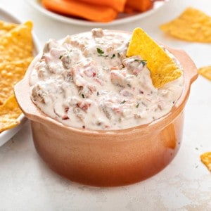 Small crock filled with spicy sausage dip with a tortilla chip in it