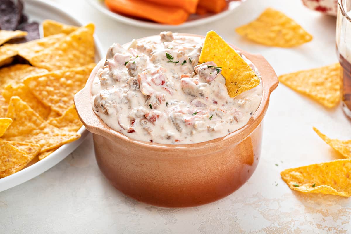 Small crock filled with spicy sausage dip with a tortilla chip in it