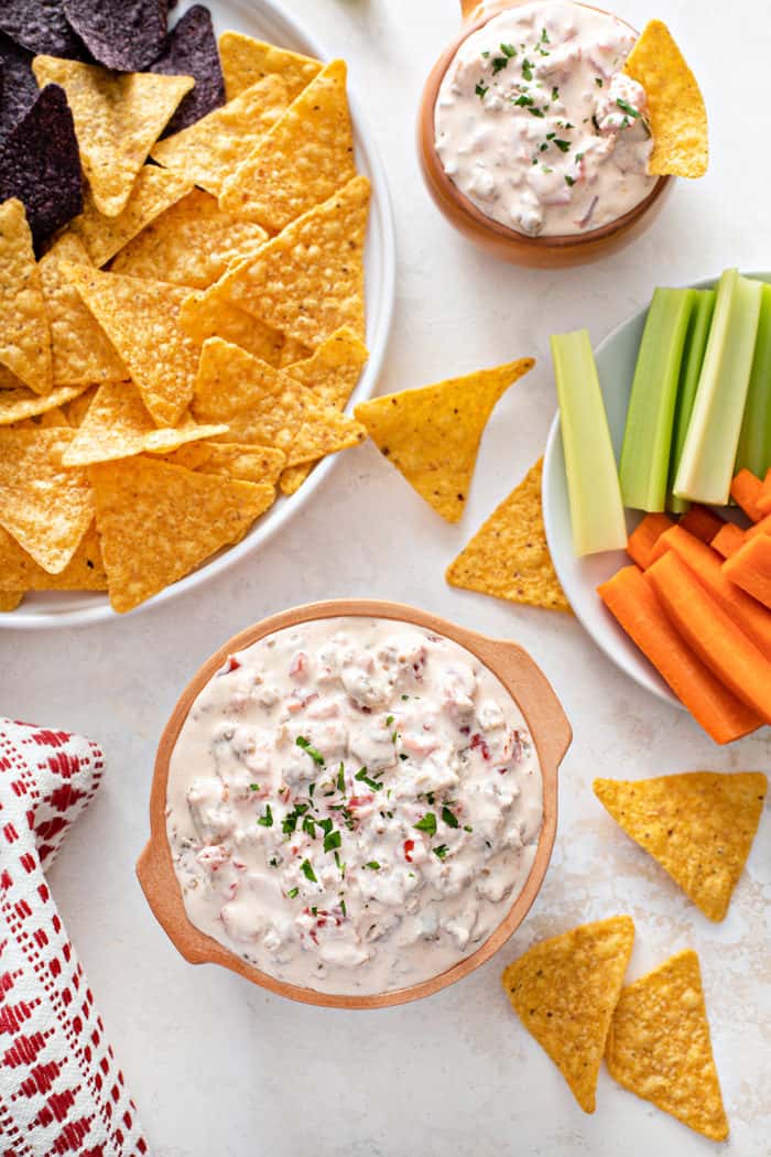 Overhead view of two bowls of spicy sausage dip surrounded by tortilla chips and fresh veggies