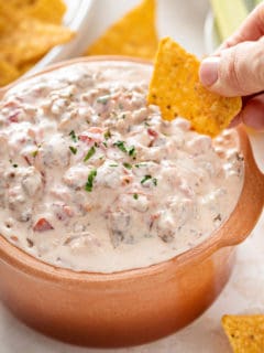 Hand scooping up spicy sausage dip with a tortilla chip