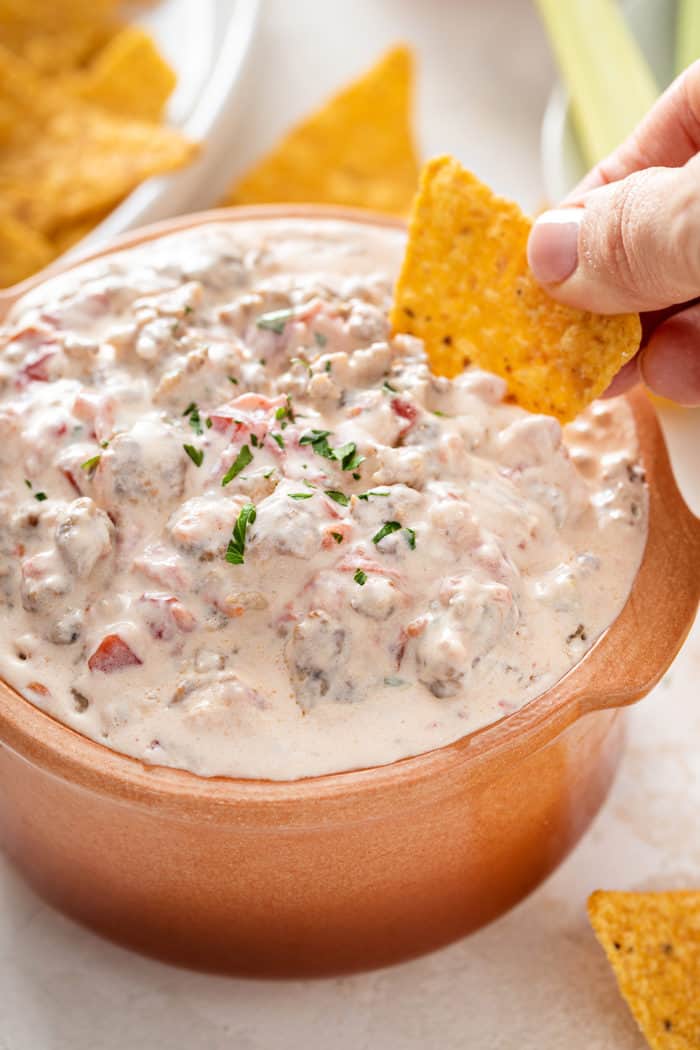 Hand scooping up spicy sausage dip with a tortilla chip