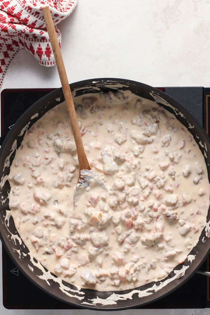 Wooden spoon stirring spicy sausage dip in a black skillet