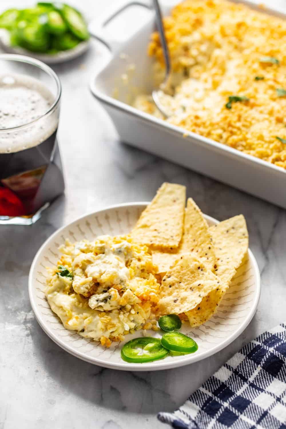 Plated jalapeno popper dip and chips next to a beer 