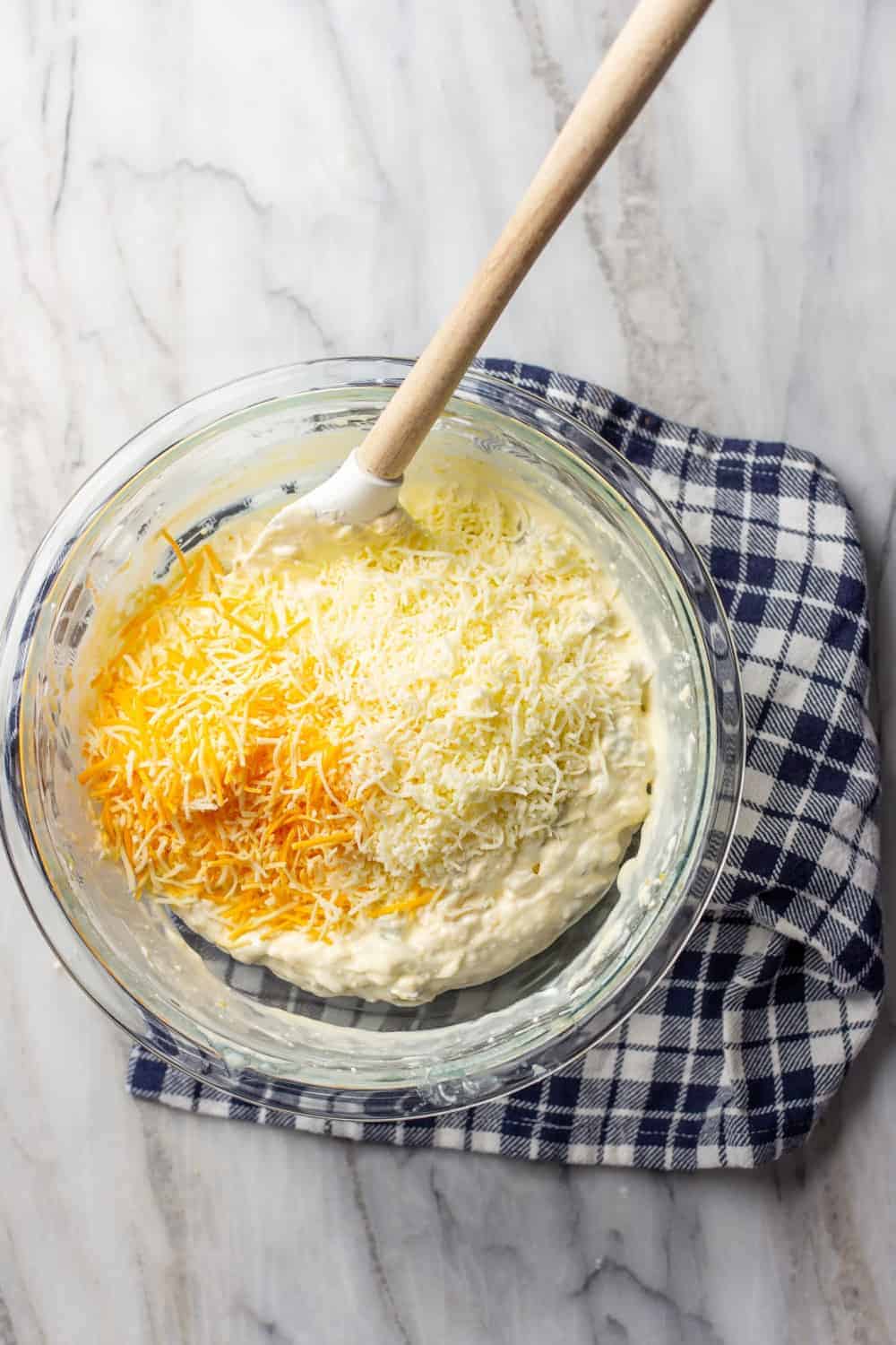 Spatula folding shredded cheese into jalapeno popper dip in a glass bowl