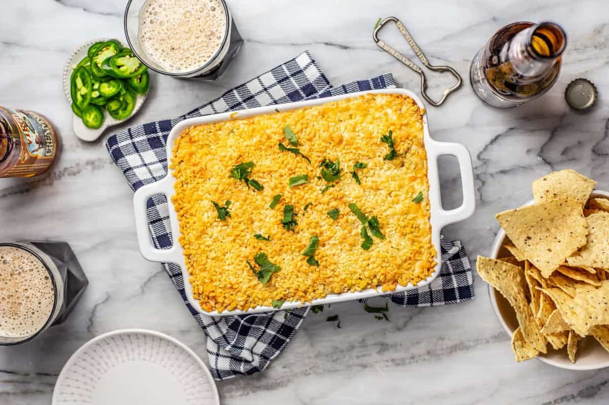 Baked jalapeno popper dip in a white baking dish surrounded by chips and beer