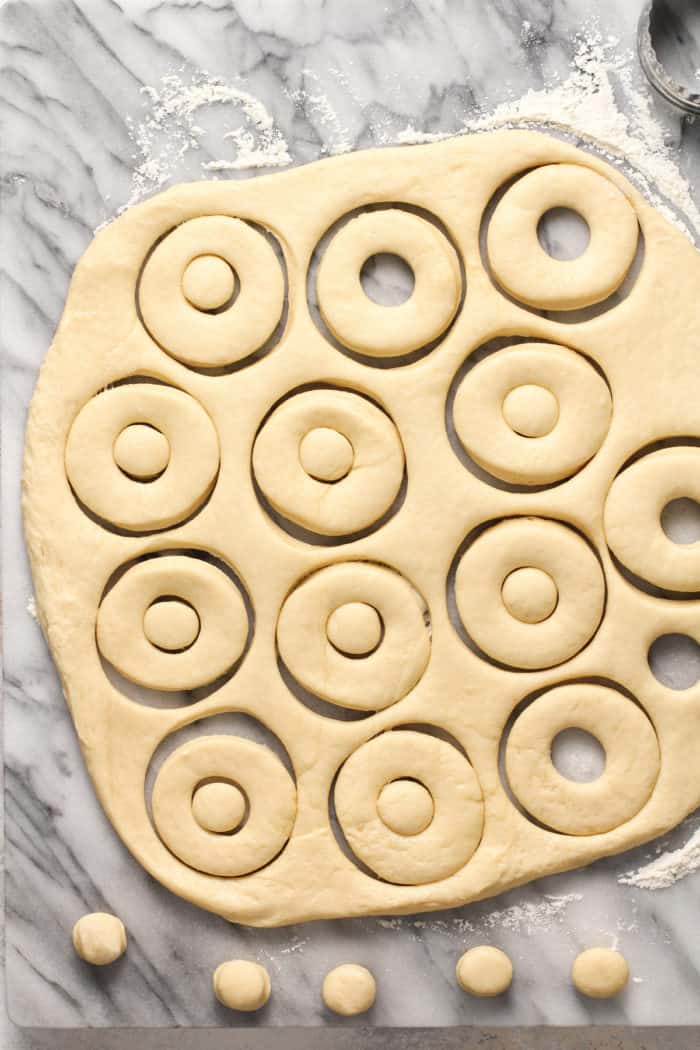 Homemade doughnuts being cut out of rolled out dough on a marble slab.