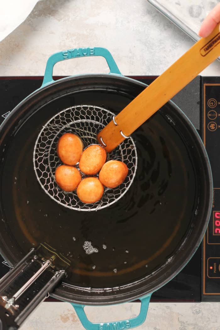 Freshly fried doughnut holes being removed from the fry oil with a metal spider.