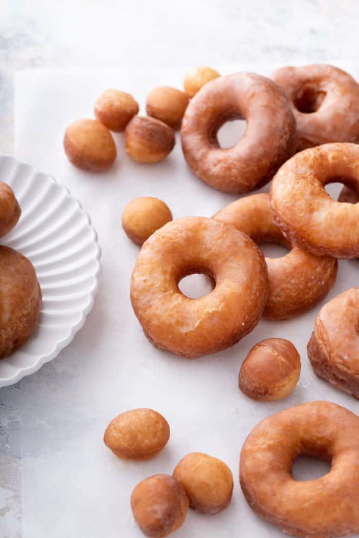 Homemade doughnuts arranged on a light-colored countertop next to a white plate.