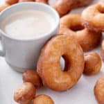 Homemade doughnut resting against the side of a cup of coffee.